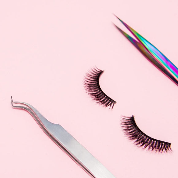 An image of long, voluminous lash extensions sitting next to tools. The background is simple, allowing the focus to remain on the lush lashes, which appear polished and glamorous.