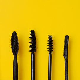 Mascara wands spread out on a bright yellow background, showcasing different brush styles for unique lash looks.