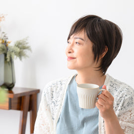 A serene Asian woman experiencing menopause enjoys a calming moment with a warm cup of tea, her gentle smile reflecting peace and self-care.