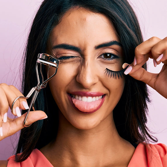 Spanish woman with natural lashes holding eyelash extensions and eyelash curler