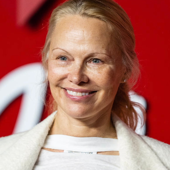 A natural, glowing Pamela Anderson sits confidently without makeup, showcasing her timeless beauty.